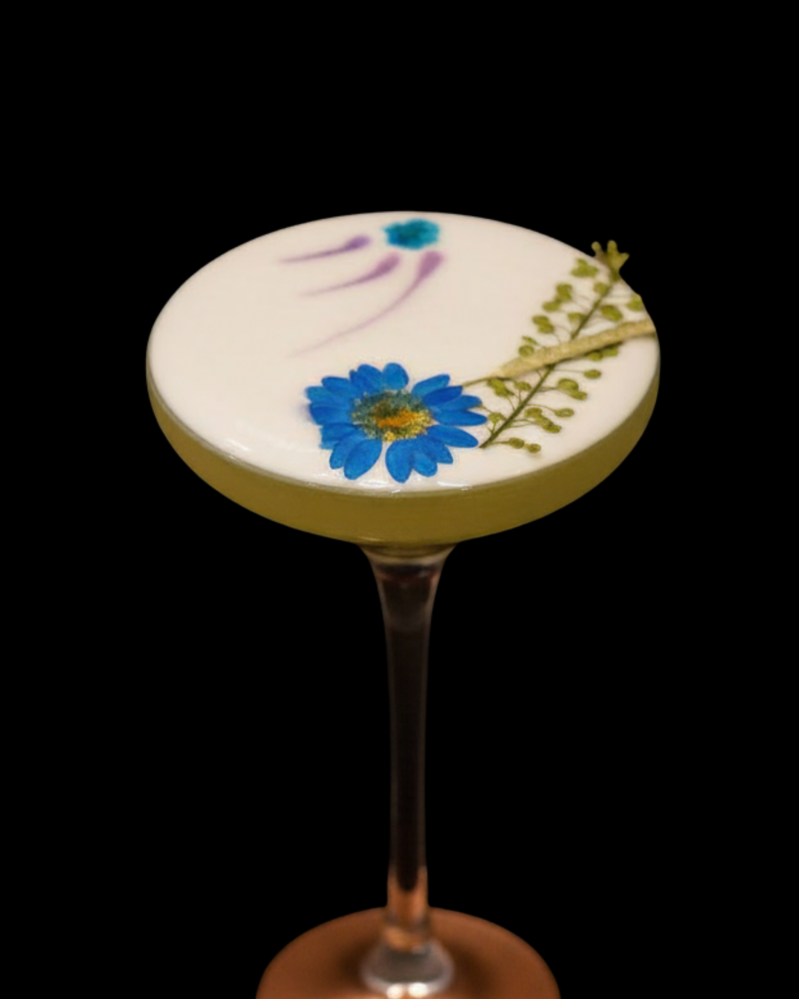 Dense white cocktail foam crown on a coupe, garnished with a blue edible flower